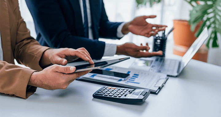 Plano detalle de manos con dispositivos electrónicos, calculadoras y hojas con gráficos