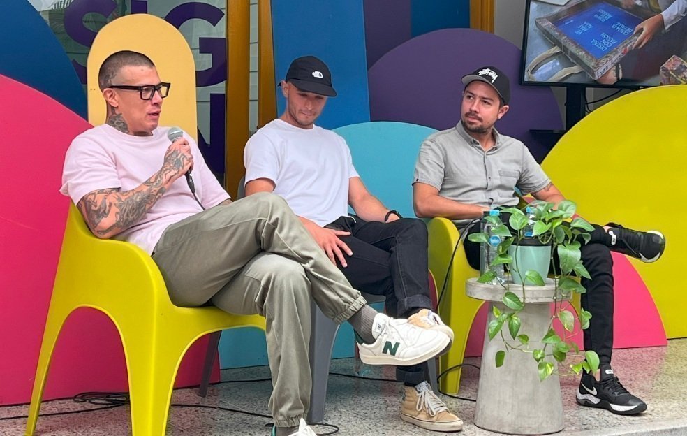 Tres hombres sentados en sillas de colores brillantes, participando en una conversación.