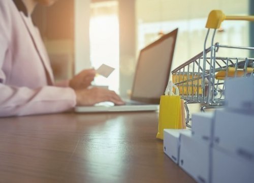 Se ve de fondo una persona sentada manipulando un computador, en primer plano se ve un carro de supermercado en versión miniatura