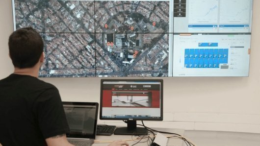 Persona monitoreando un sistema en un centro de control con pantallas de mapas y datos.