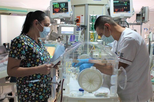 Personal médico atendiendo a un recién nacido en incubadora en una sala UCI neonatal.