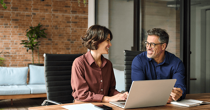 Plano medio de dos personas sentadas con un computador y sonriendo